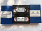 Two vintage VHS tapes with blue jewel cases are stacked vertically on a white surface with soft leaf shadows. The center tape is open, showing the black plastic tape reels inside, and both tapes feature white labels with text and a BMW logo.